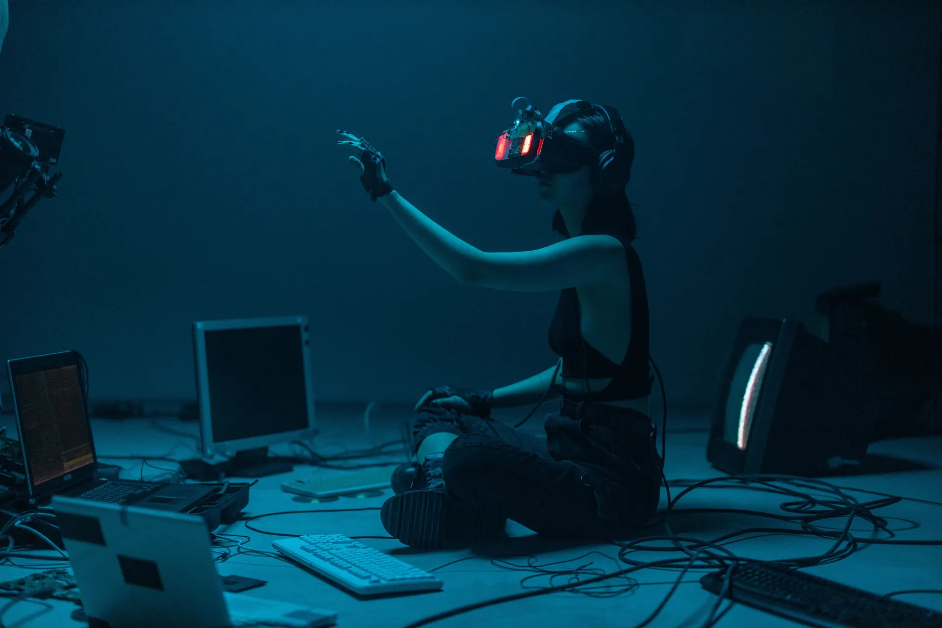 Person wearing a VR headset in a dim teal room surrounded by old computers