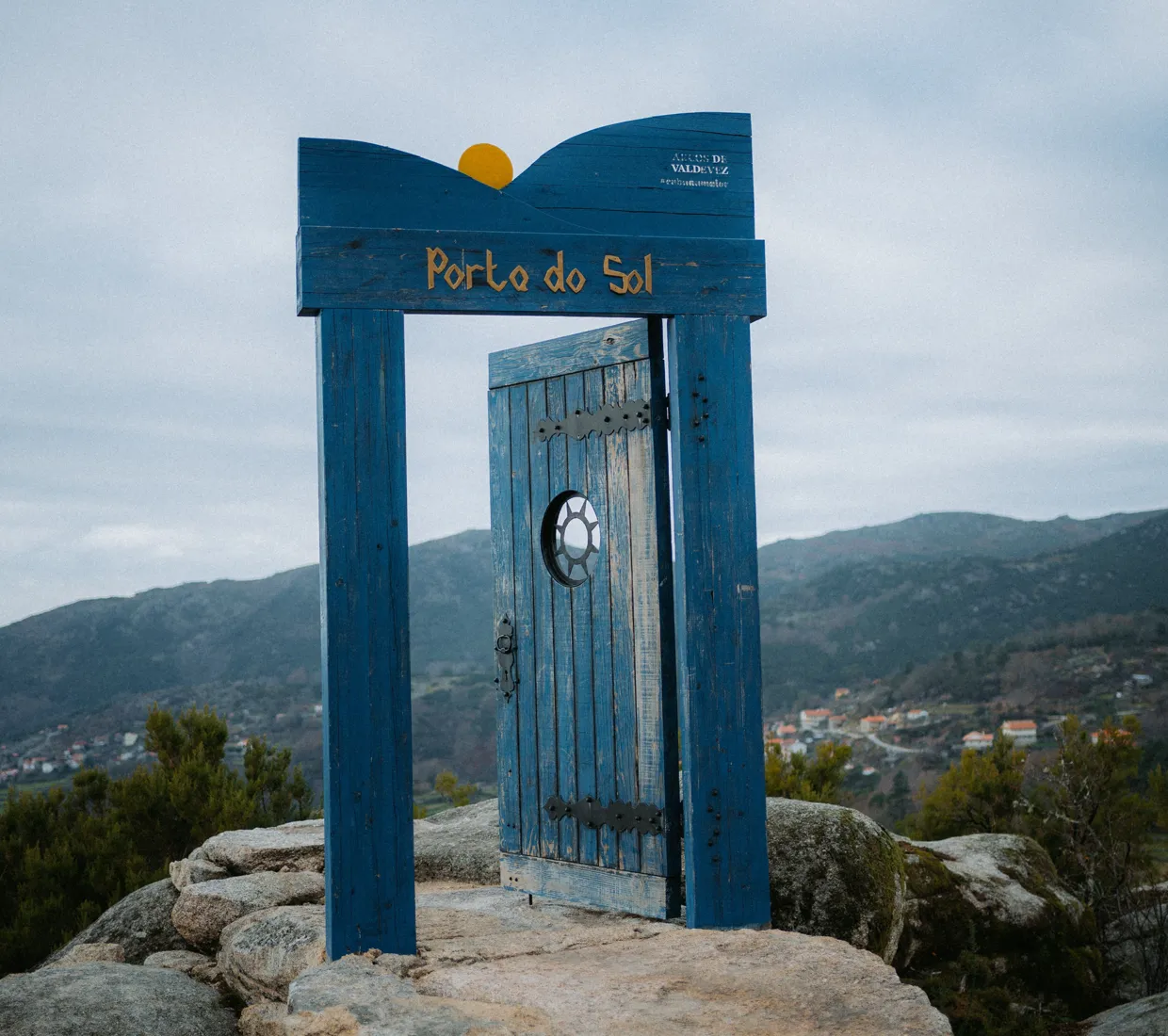 A blue standalone doorway on a rocky hilltop overlooking the valley