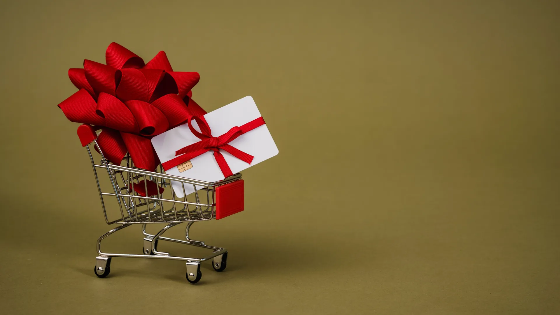 A gift card tied with a red bow in a miniature shopping cart